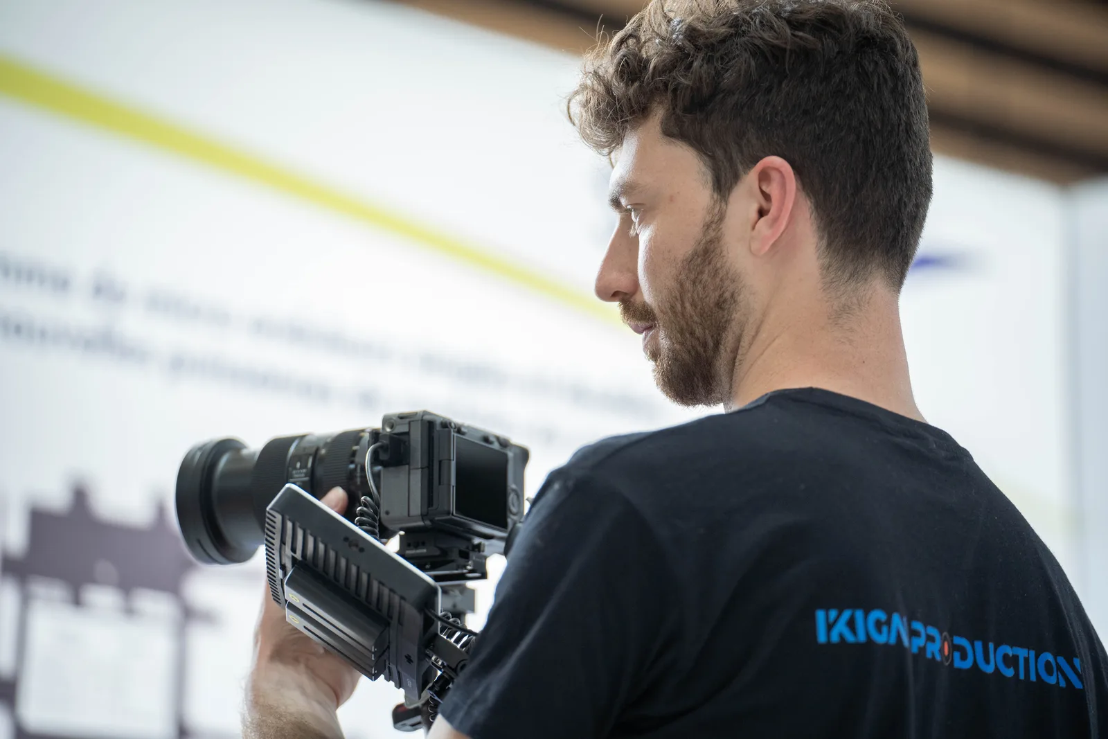 Vidéaste qui filme à l'épaule sur un salon professionnel, au milieu des entreprises exposantes